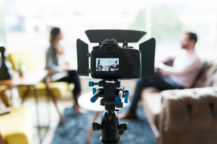 Reporter interviewing businessman seen on video camera display at office