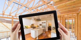 Female Hands Holding Computer Tablet with Finished Kitchen on Screen, Construction Framing Behind.