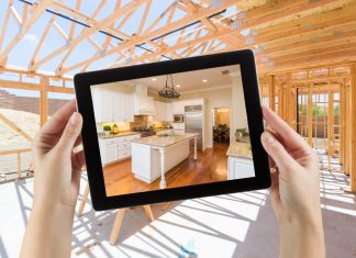 Visualization tools help builders engage clients, save time and reduce costs Female Hands Holding Computer Tablet with Finished Kitchen on Screen, Construction Framing Behind.