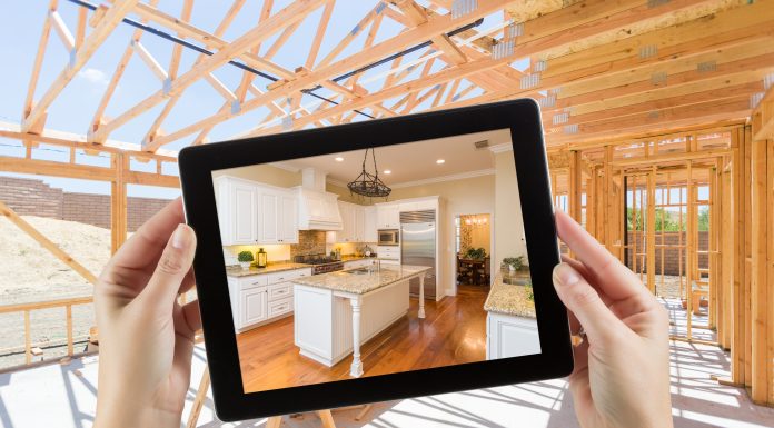 Visualization tools help builders engage clients, save time and reduce costs Female Hands Holding Computer Tablet with Finished Kitchen on Screen, Construction Framing Behind.