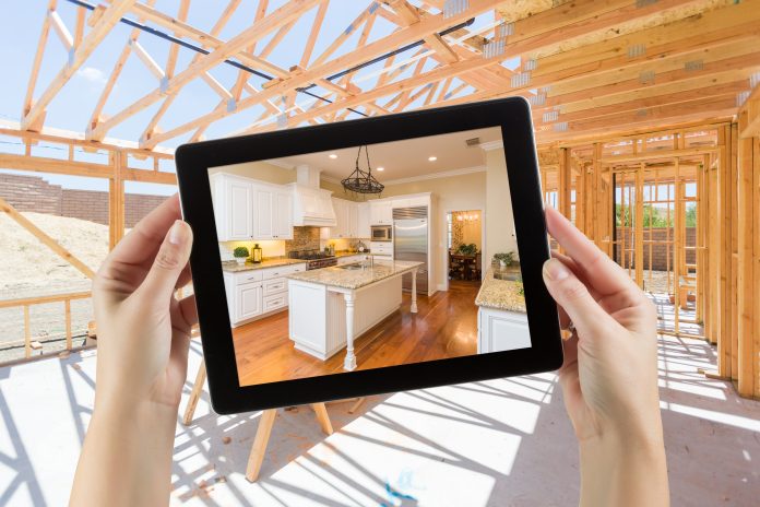 Female Hands Holding Computer Tablet with Finished Kitchen on Screen, Construction Framing Behind.