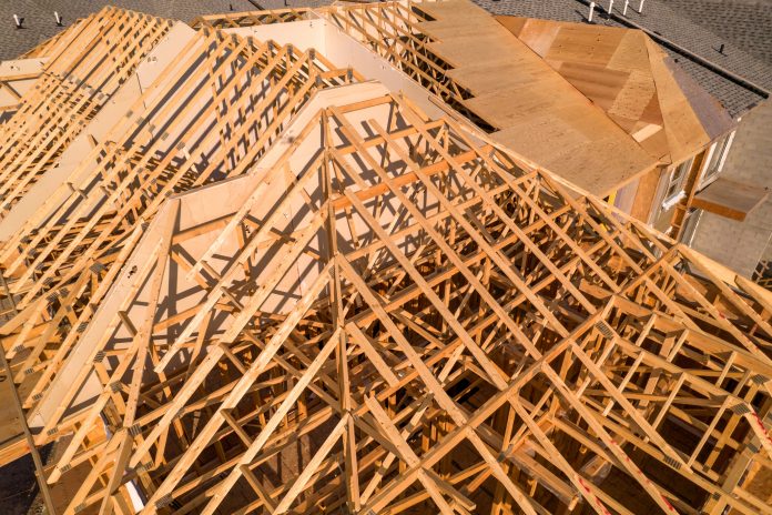 Roofing construction aerial. Wooden roof frame installation of the house. Truss beams structures on new home view from above. Golden hour. House or family home construction and real estate.