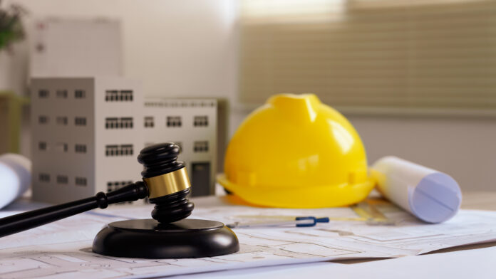 Judge gavel on building blueprint plans with a yellow safety helmet in the background. law that deals with matters relating to building construction, engineering. Construction law concept.