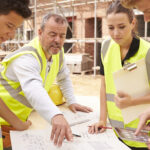 Builder On Building Site Discussing Work With Apprentice